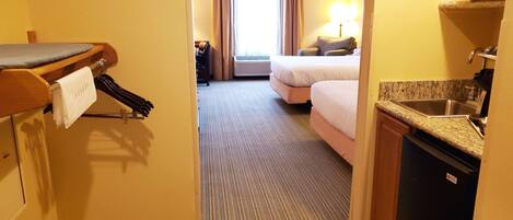 Habitación de hotel con cama, escritorio con silla, televisor, lavamanos y ventana con cortinas.
