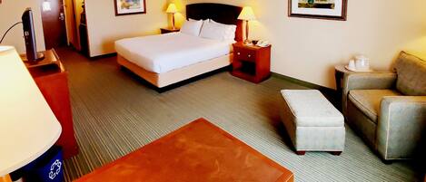 A hotel room with a bed, a desk, a chair, a sofa, and a small table.
