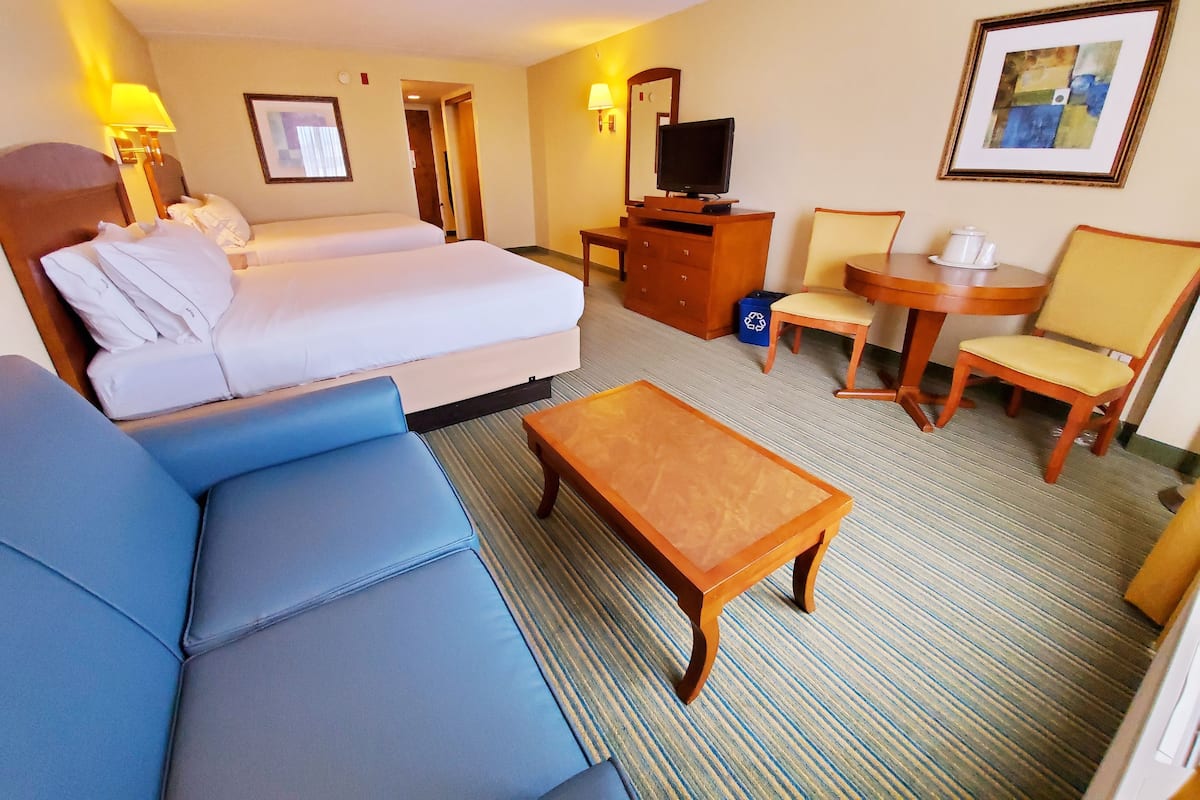 A hotel room with a bed, a sofa, a coffee table, a TV, a desk, and a chair.