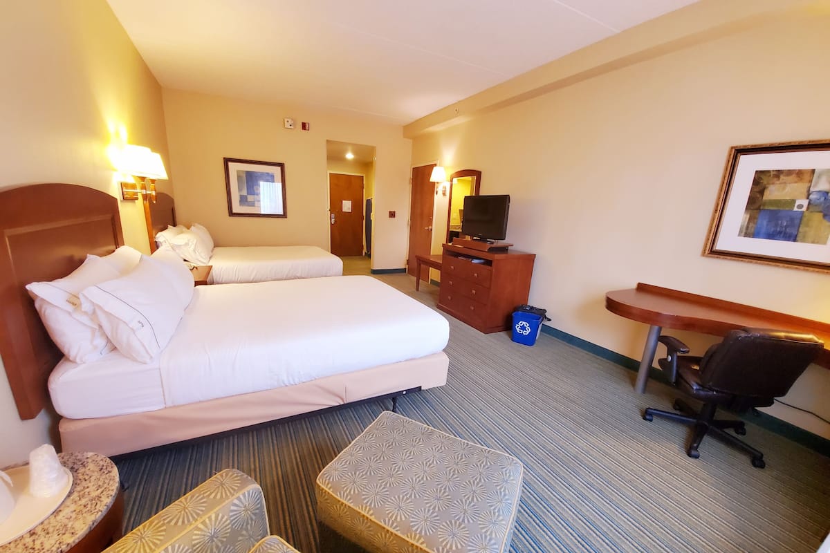 A hotel room with two beds, a desk, a chair, a television, and a framed picture on the wall.