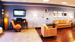 A hotel lobby with a sofa, chairs, a TV, artwork, and a kitchen area. - Beach Boutique Hotel (Rehoboth Beach)