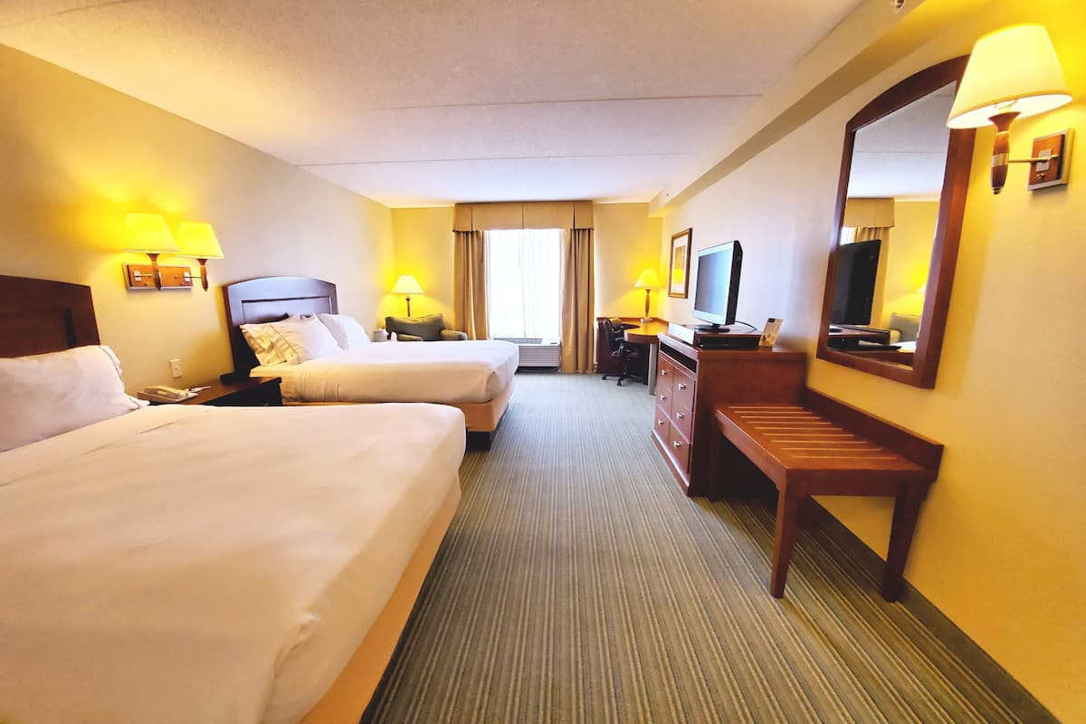 A hotel room with two beds, a desk, a chair, a television, and a mirror.