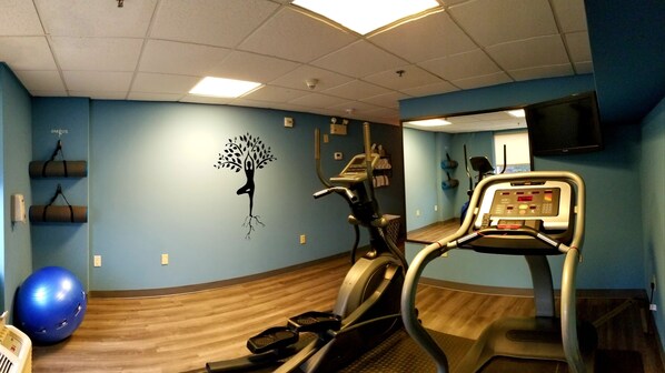 A fitness room with exercise equipment, a blue wall, and a wooden floor.