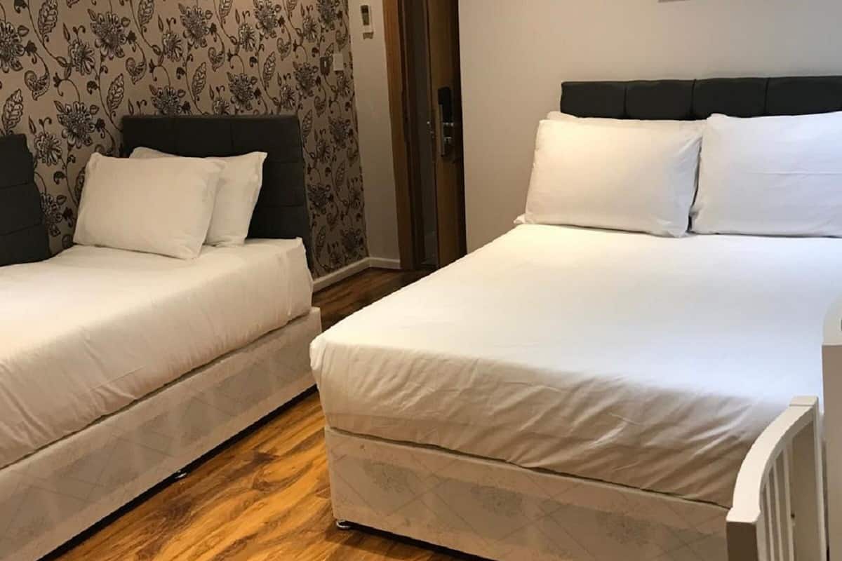 A hotel room with two single beds, a wooden floor, and a patterned rug.