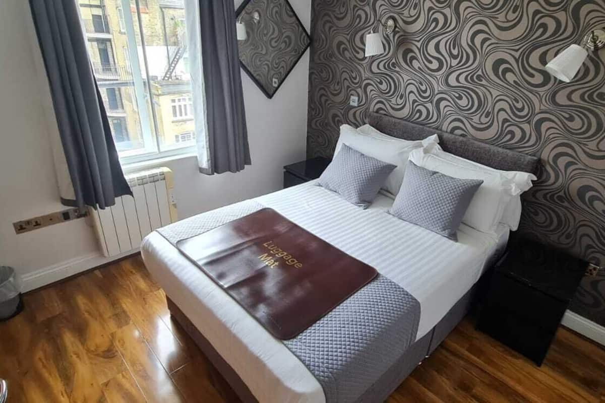A neatly arranged bedroom with a bed, pillows, a bedside table, a radiator, and a window with curtains.