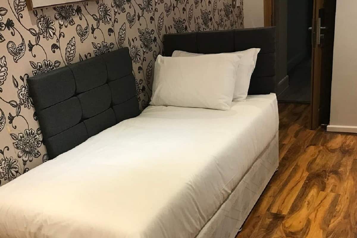A bedroom with a bed, a dark headboard, and a floral wallpaper pattern.