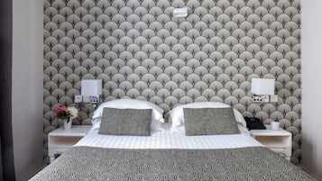 Una cama bien tendida con ropa de cama estampada, dos mesitas de noche con lámparas y una pared con un diseño geométrico repetido.
