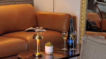 A modern living room with a leather sofa, a glass coffee table, a lamp, a bottle of wine, and a glass of wine.