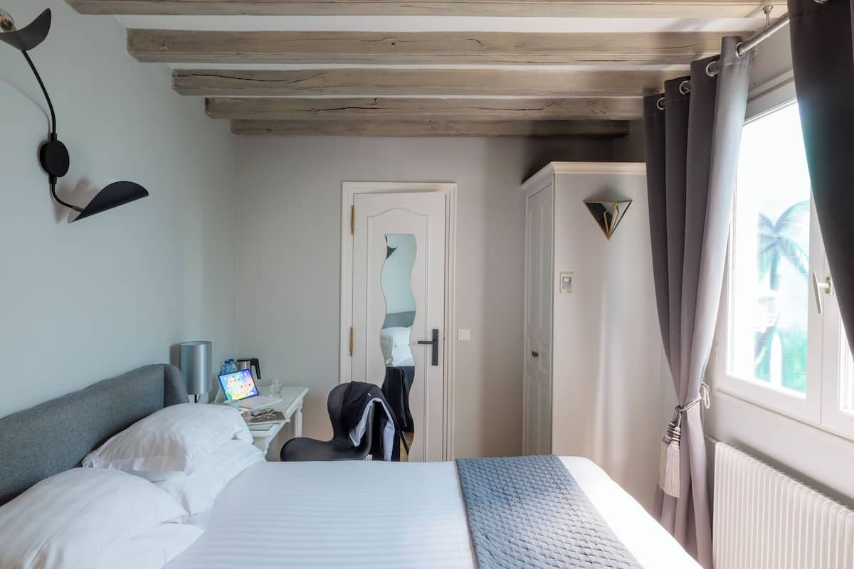 A hotel room with a bed, a desk with a computer, a wardrobe, and a window with curtains.