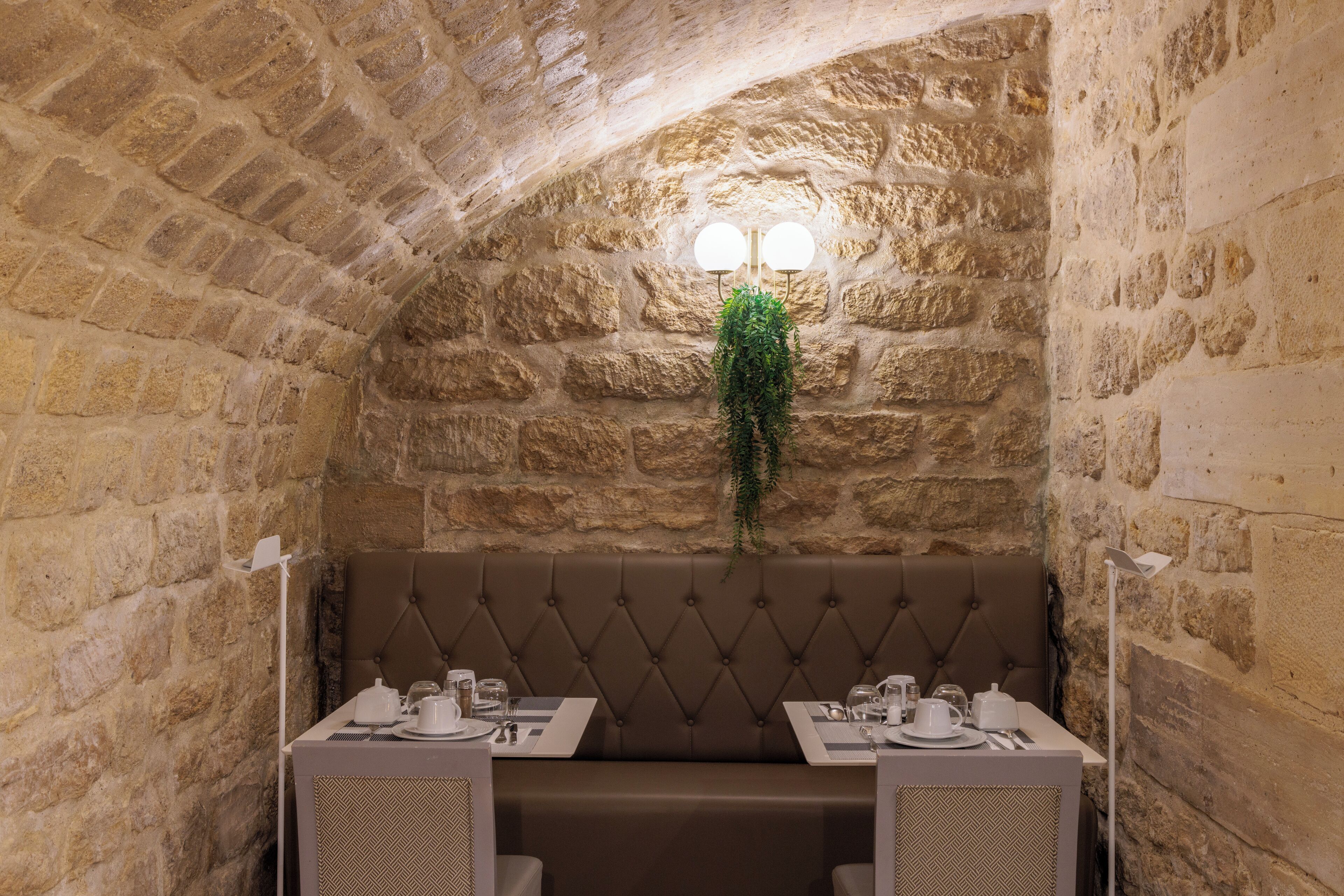 Comedor de paredes de piedra con un banco acolchado y dos mesas dispuestas para comer, cada una con platos, vasos y cubiertos.