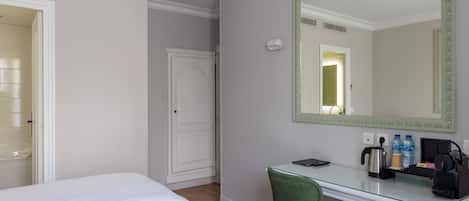 A hotel room with two beds, a desk, a chair, a mirror, a kettle, and a small trash bin.