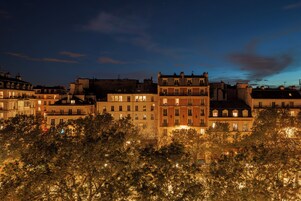 Vista nocturna de una hilera de edificios de varios pisos con ventanas iluminadas, rodeados de árboles.
