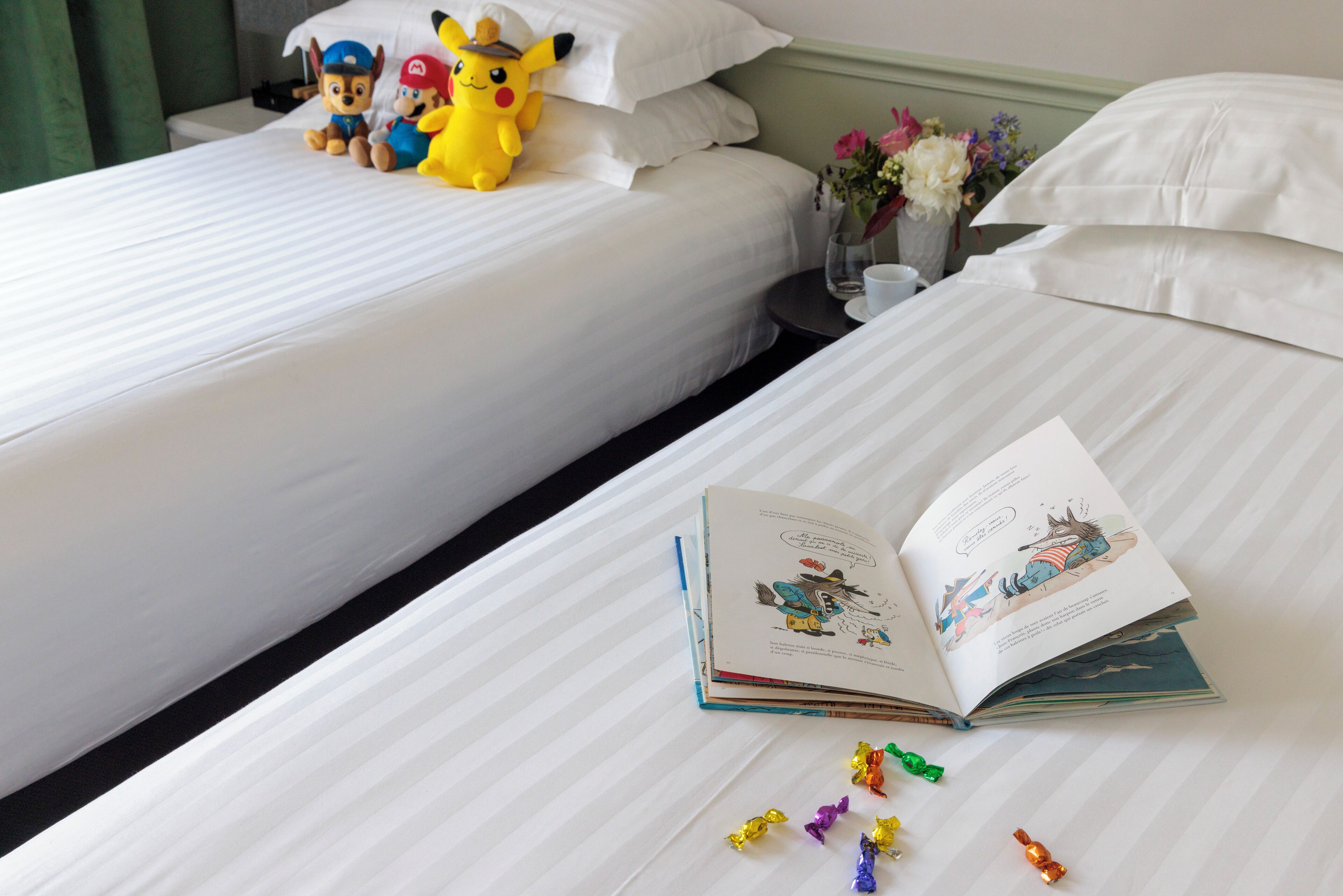 Habitación de hotel con dos camas, un libro y peluches en una de ellas.