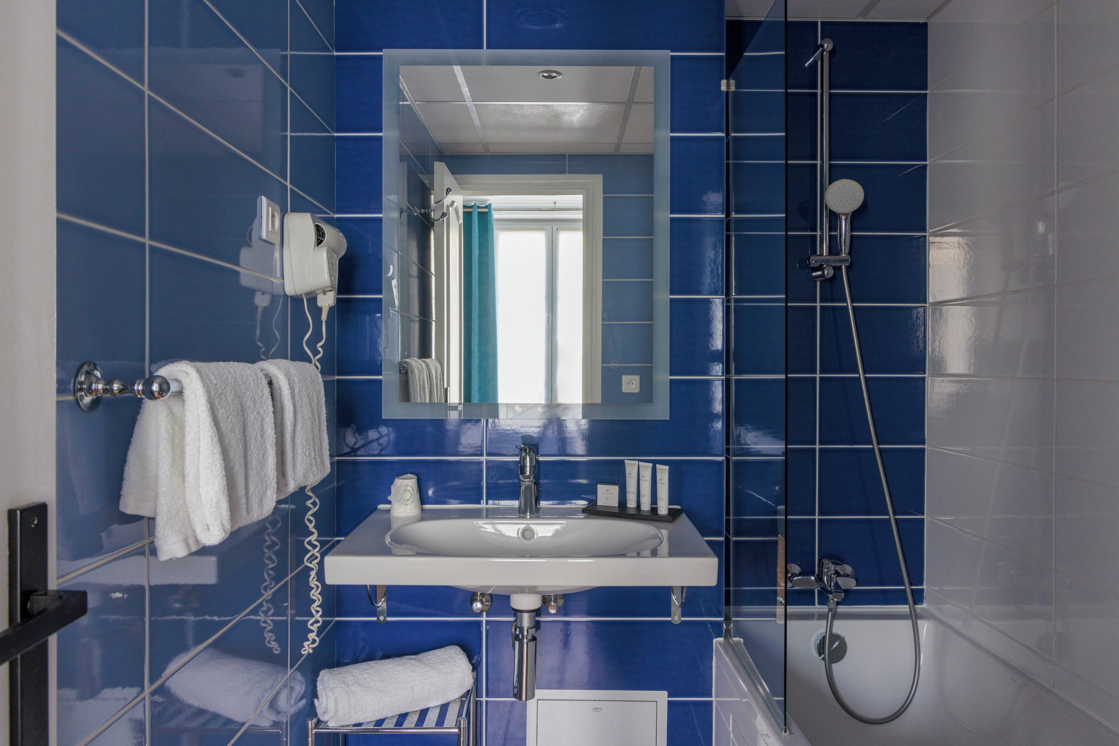 Une salle de bain avec un lavabo blanc, des carreaux bleus, un miroir, un porte-serviettes et une douche.