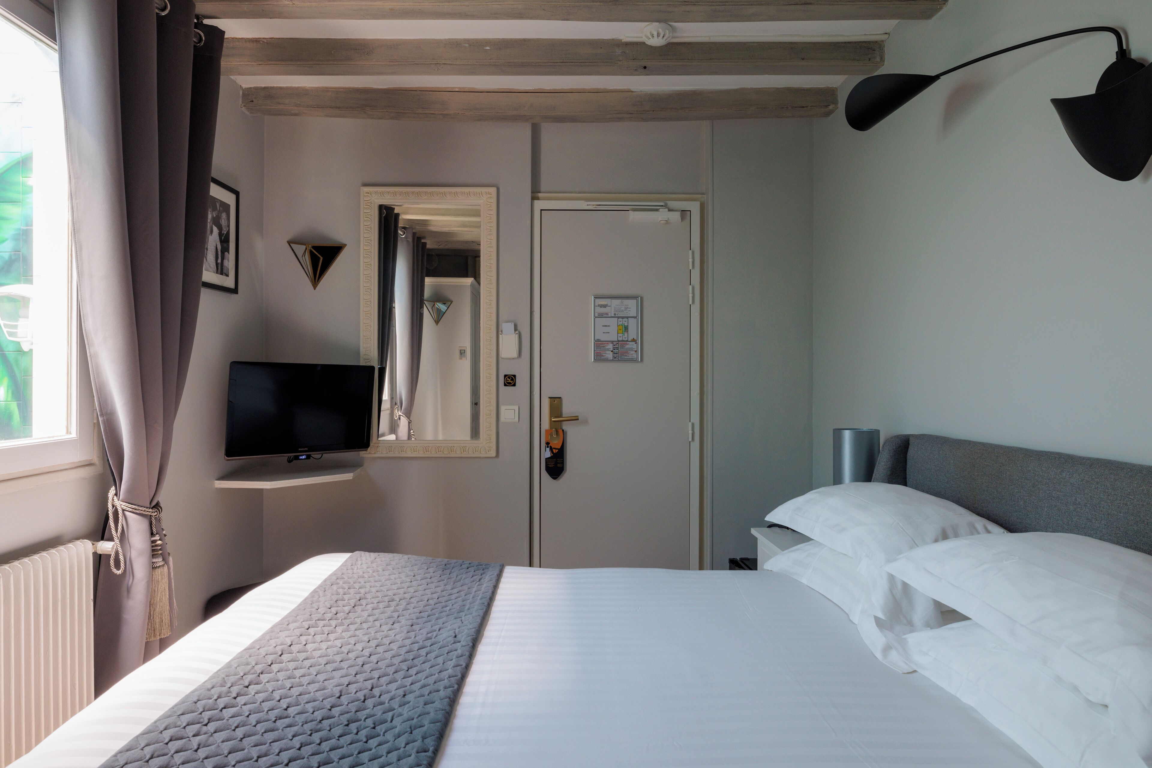 Une chambre d’hôtel avec un lit, un téléviseur posé sur un meuble, une porte et une lampe fixée au mur.