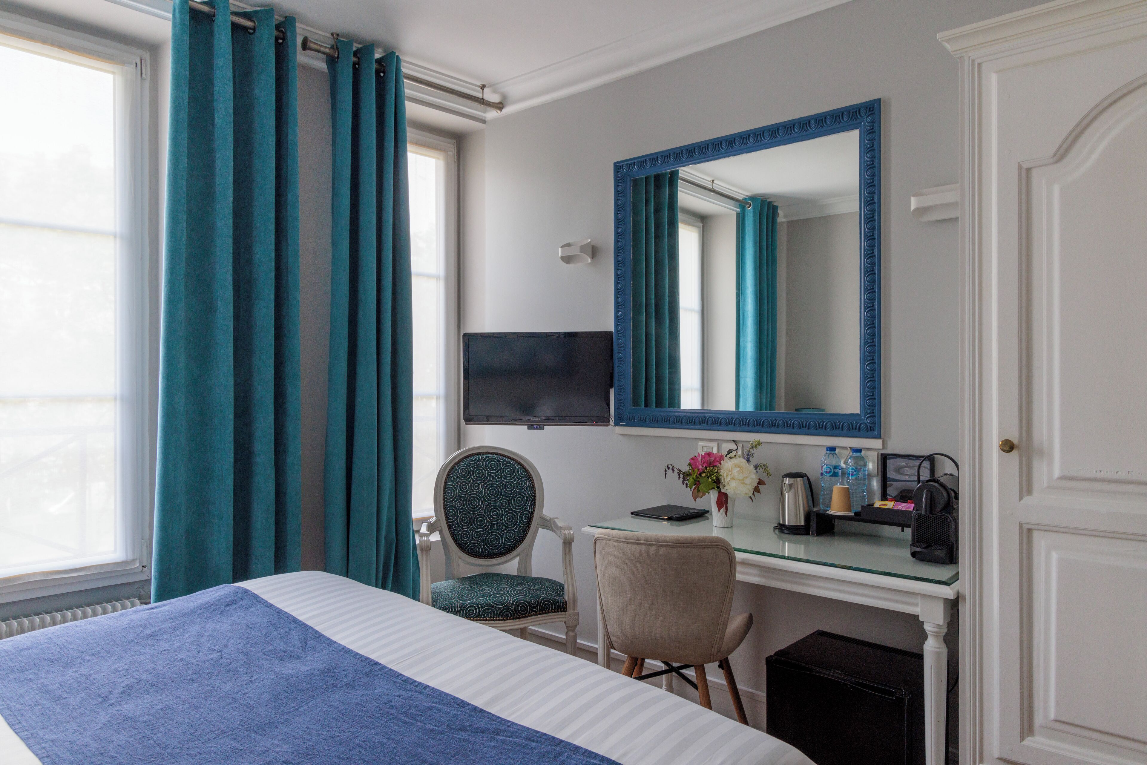 A hotel room with a bed, a desk, a chair, a television, and a mirror.
