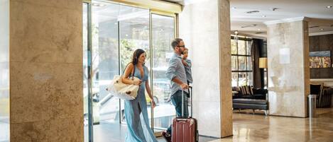 A spacious lobby with a marble floor, a glass entrance, and a seating area with a sofa and armchairs.