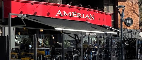 Un restaurante llamado AMERIAN con terraza y un edificio de ladrillo al fondo.