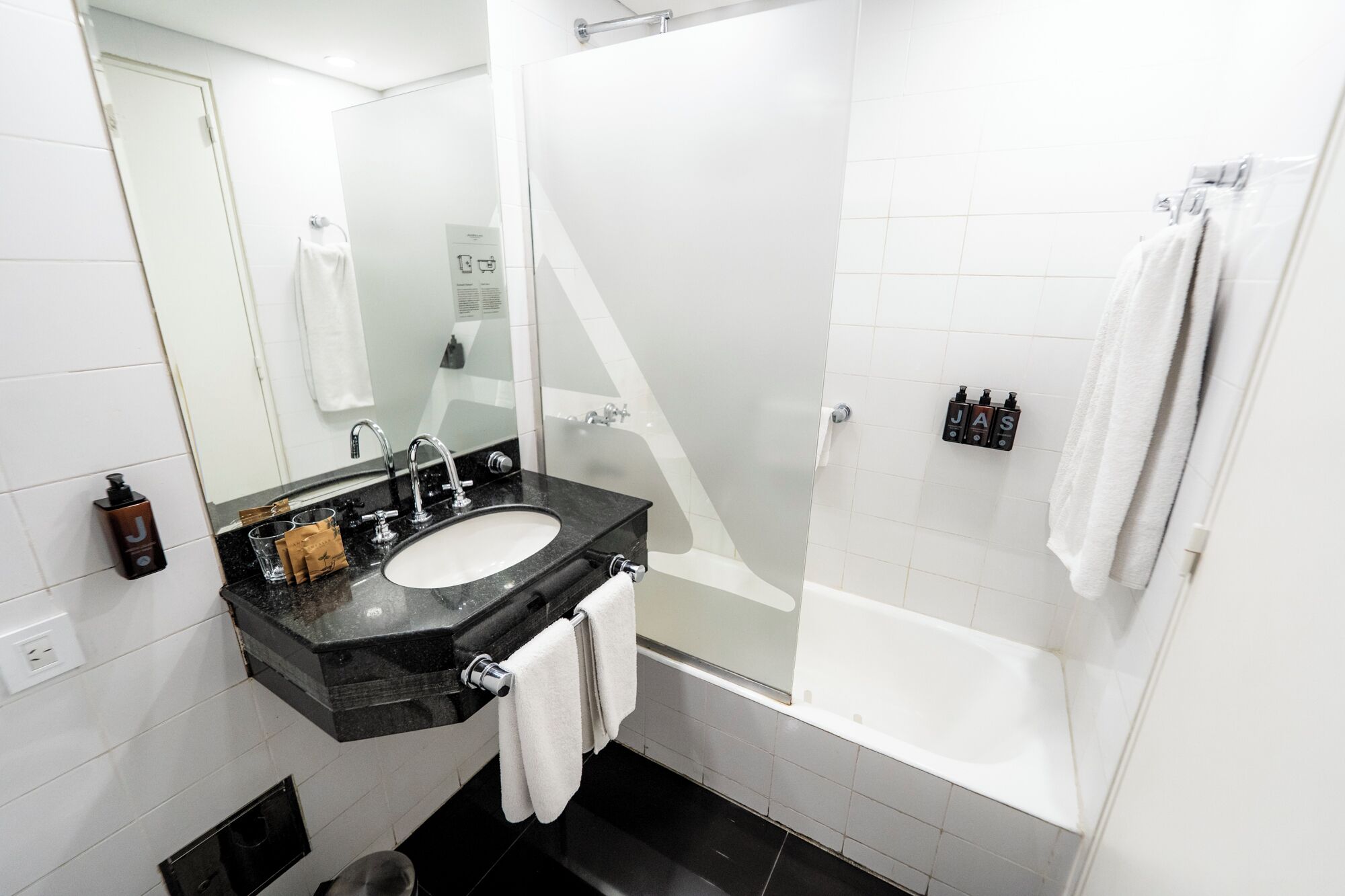 A modern bathroom with a black sink, a mirror, a glass shower enclosure, and a white bathtub.