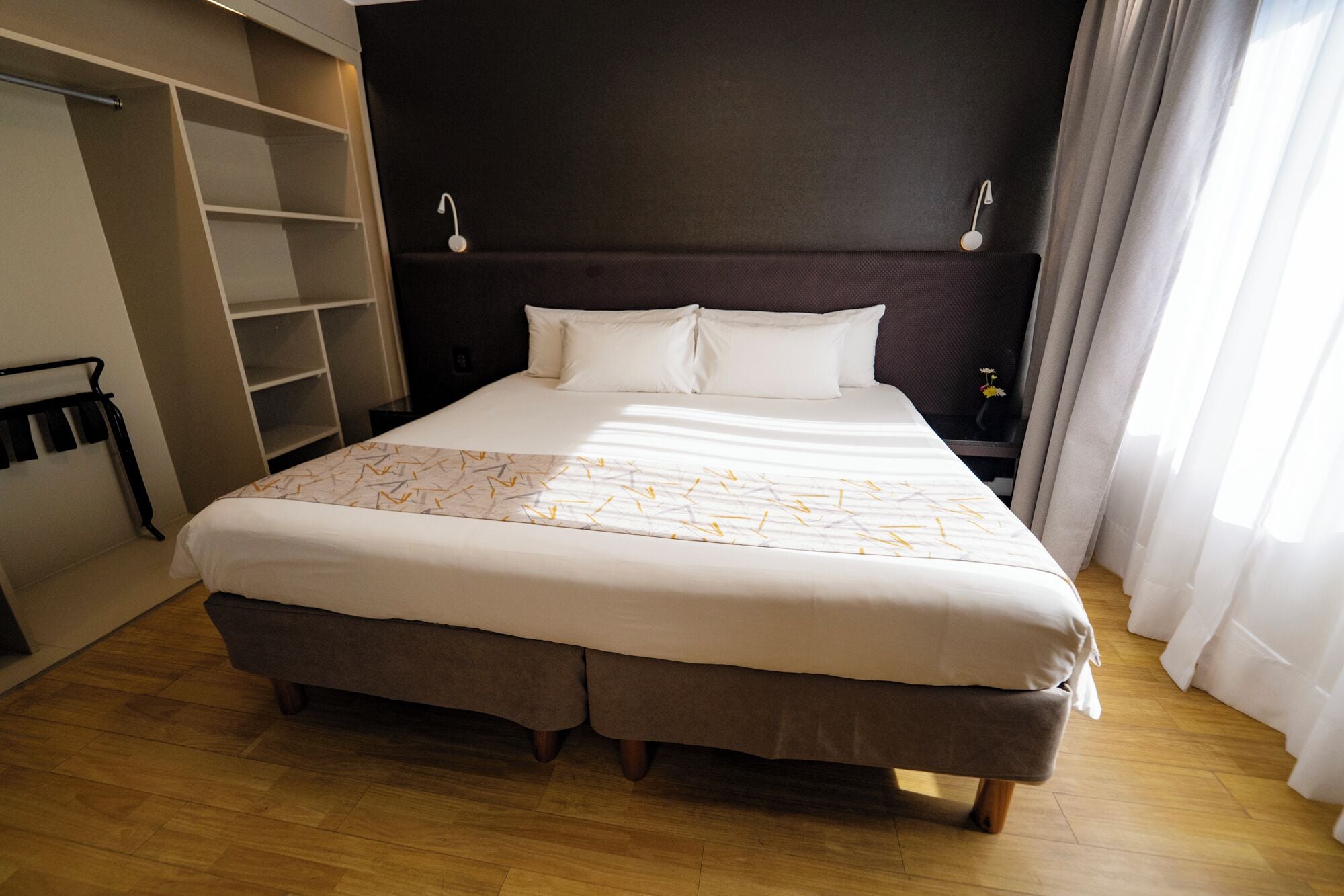A hotel room with a large bed, a wardrobe, a nightstand, and a window with curtains.