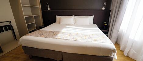 A hotel room with a large bed, a wardrobe, a nightstand, and a window with curtains.