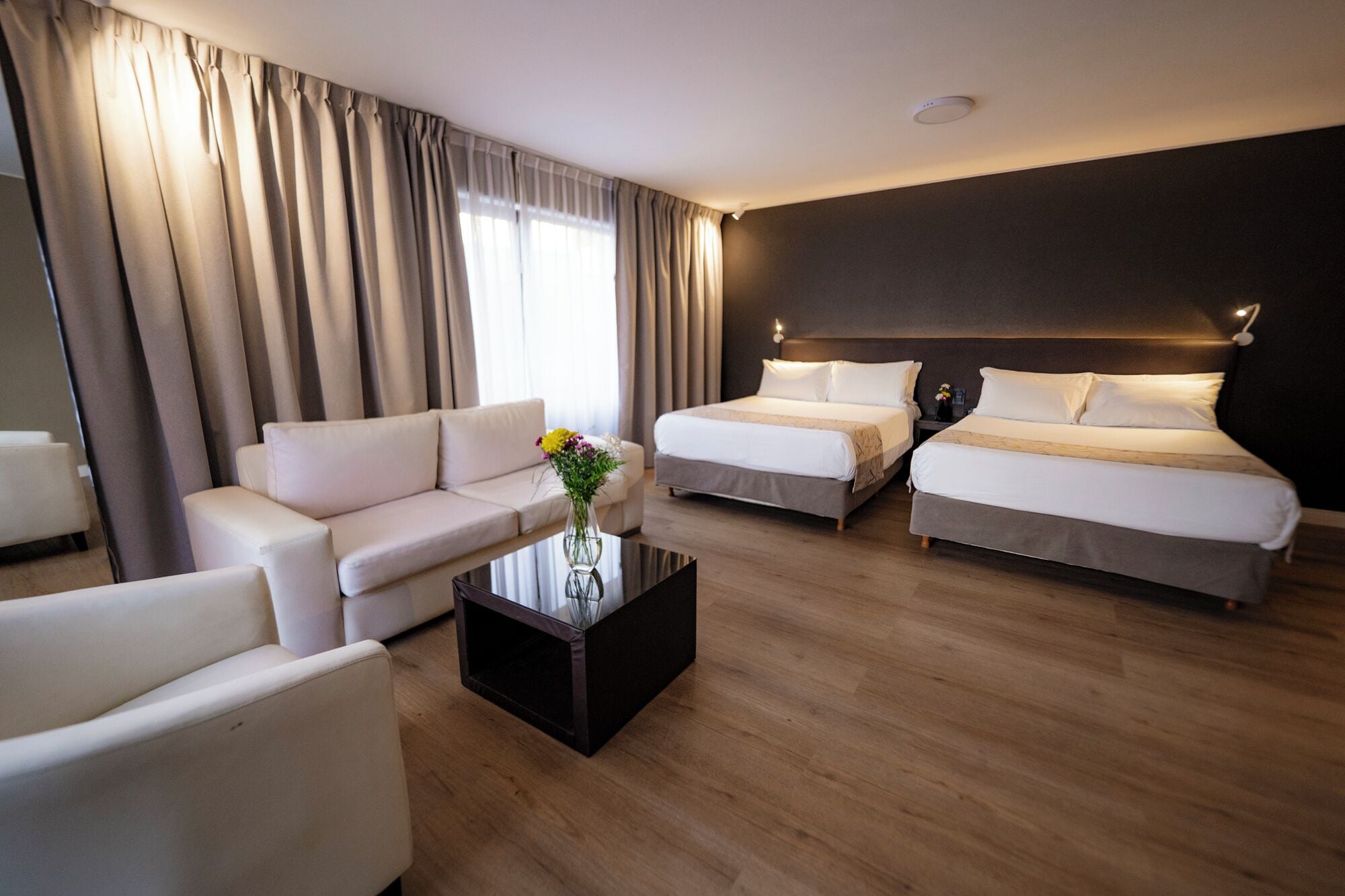 Habitació d'hotel amb un sofà, dos llits, una taula de cafè i un ram de flors.