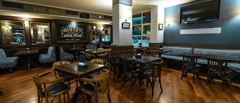 A restaurant interior with wooden tables and chairs, a bar area, and a large TV screen on the wall.