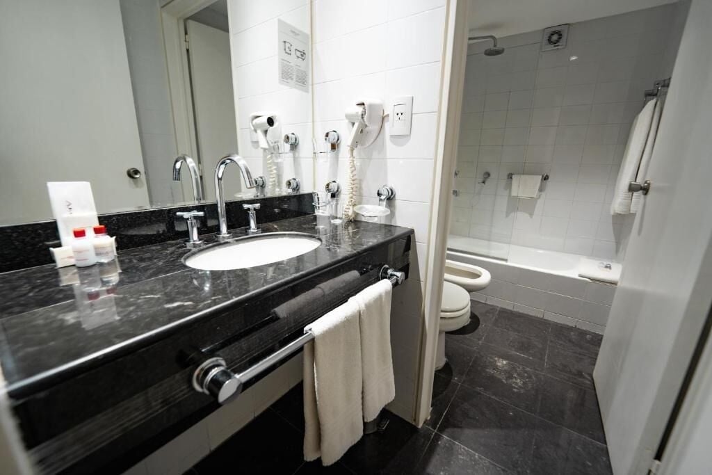 Une salle de bain moderne avec un lavabo en marbre noir, un miroir, un sèche-cheveux, des toilettes et un espace douche.