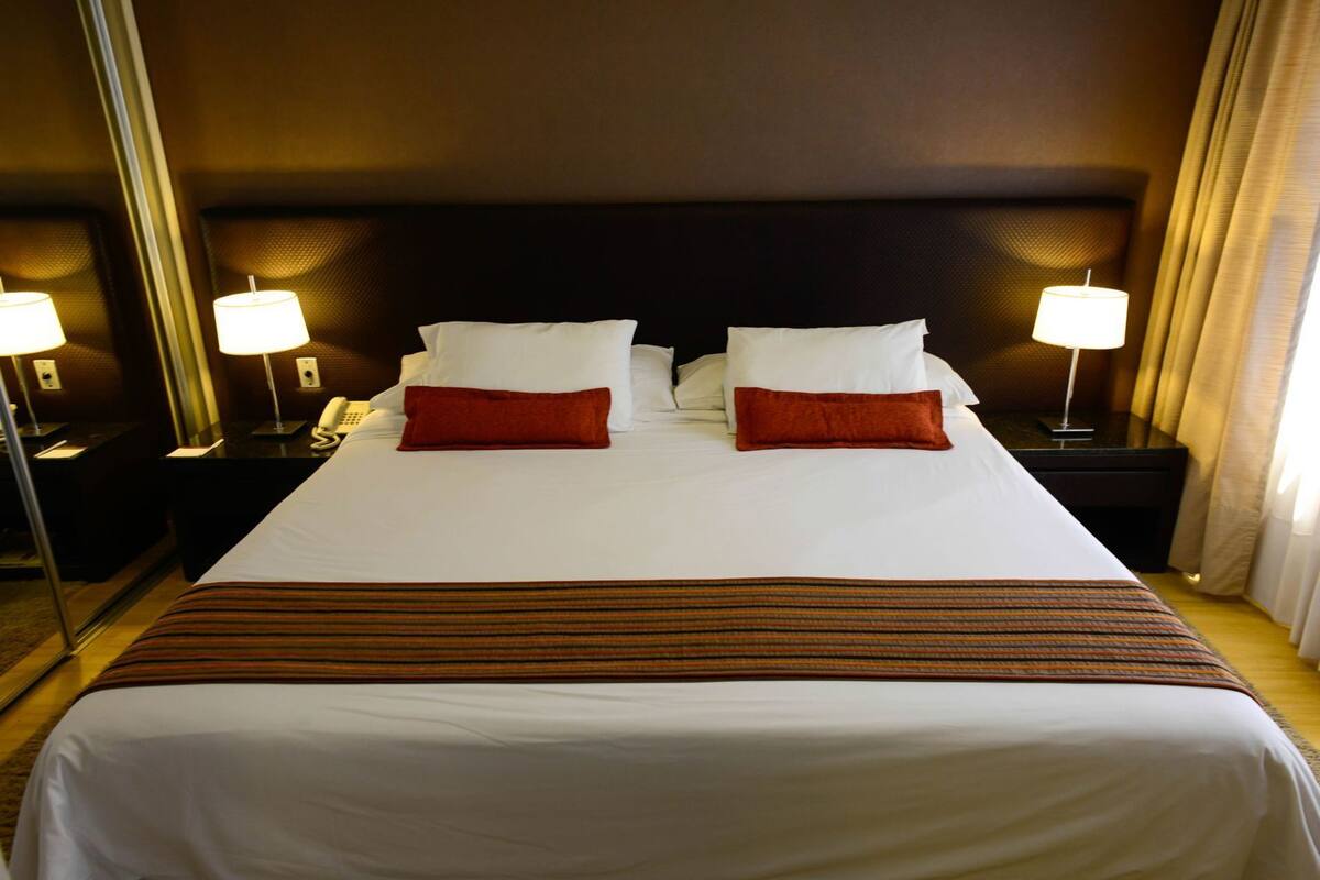 A hotel room with a large bed, two bedside tables, a telephone, and two lamps.