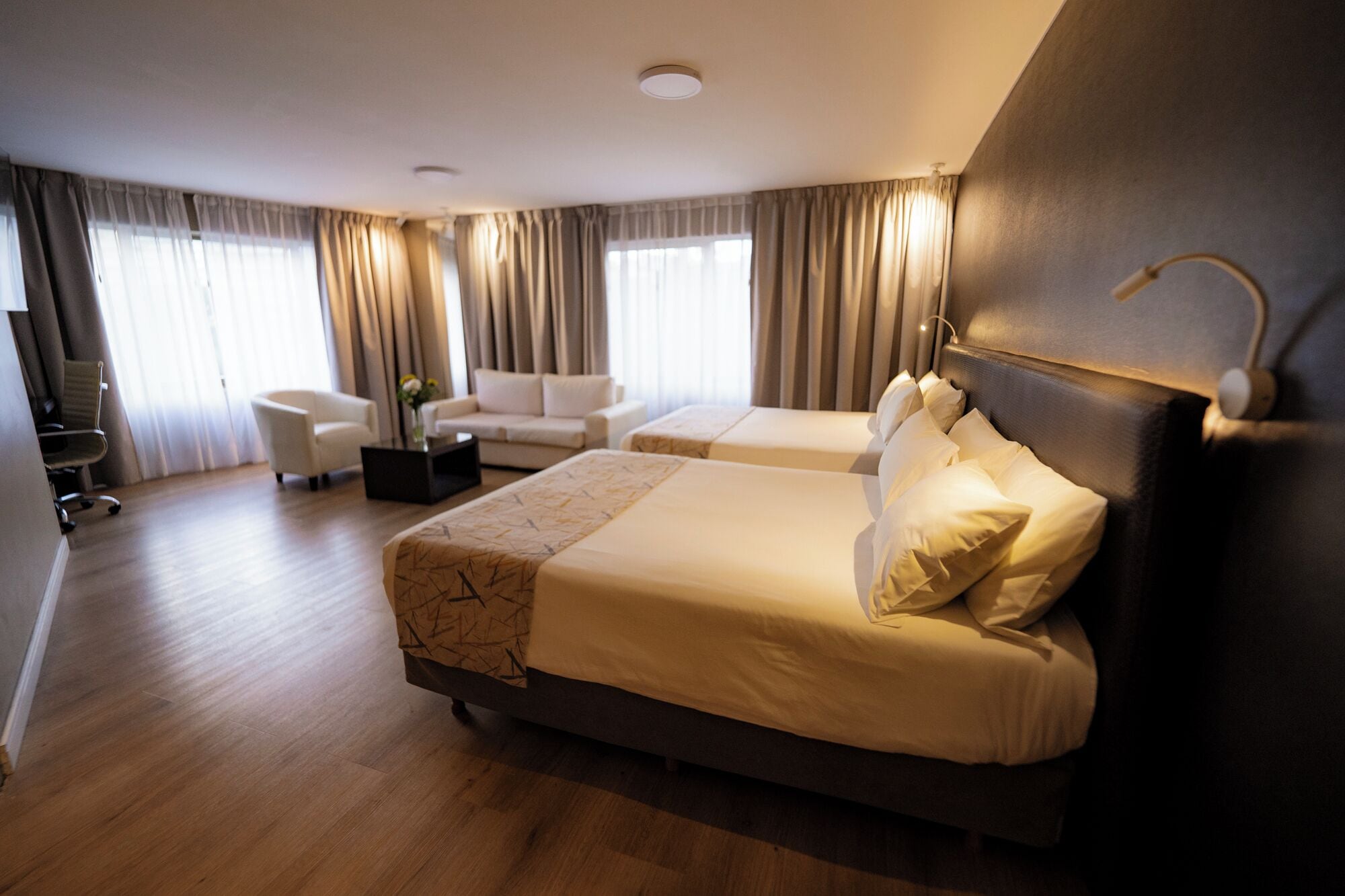 A hotel room with two beds, a sofa, a coffee table, and a desk.