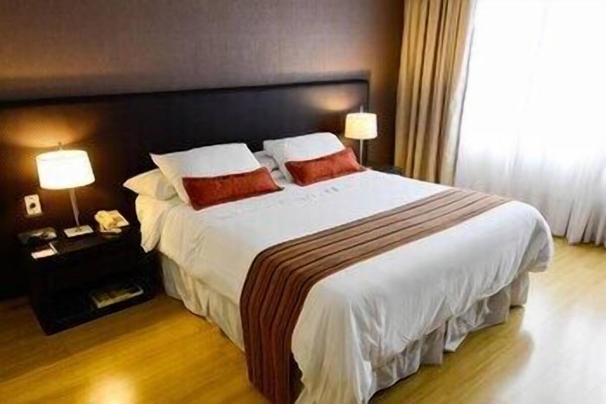 A hotel room with a bed, nightstands, lamps, and a window with curtains.