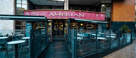 An outdoor seating area of a restaurant with a glass enclosure and a covered patio.