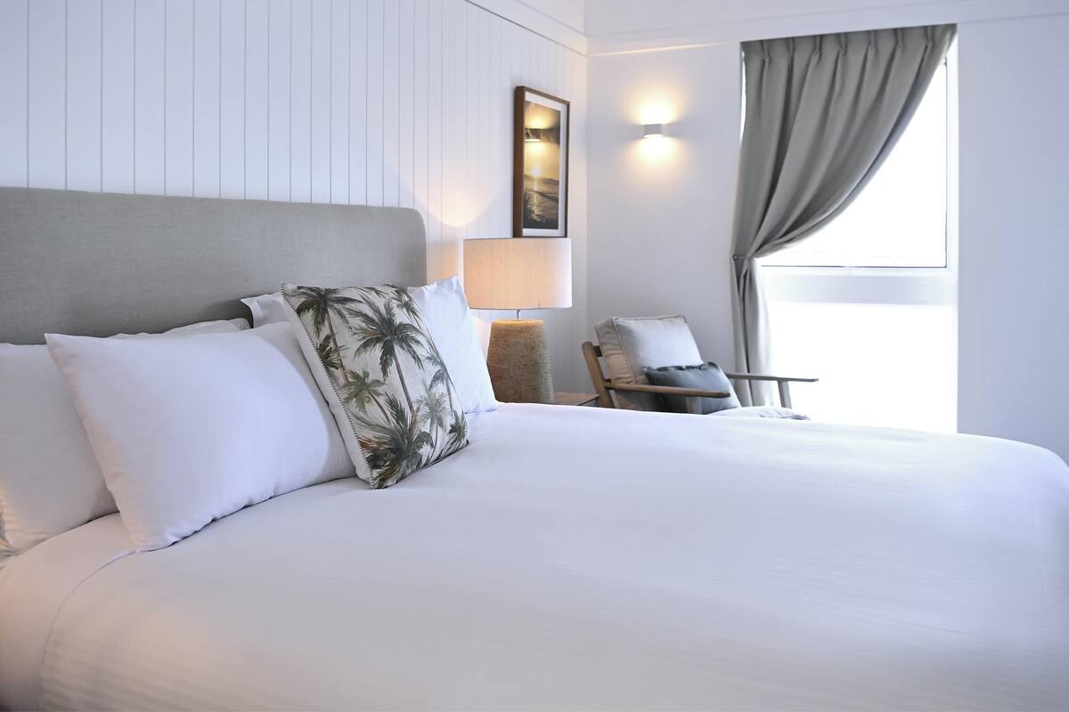 A hotel room with a large bed, a chair, a lamp, and a window with curtains.