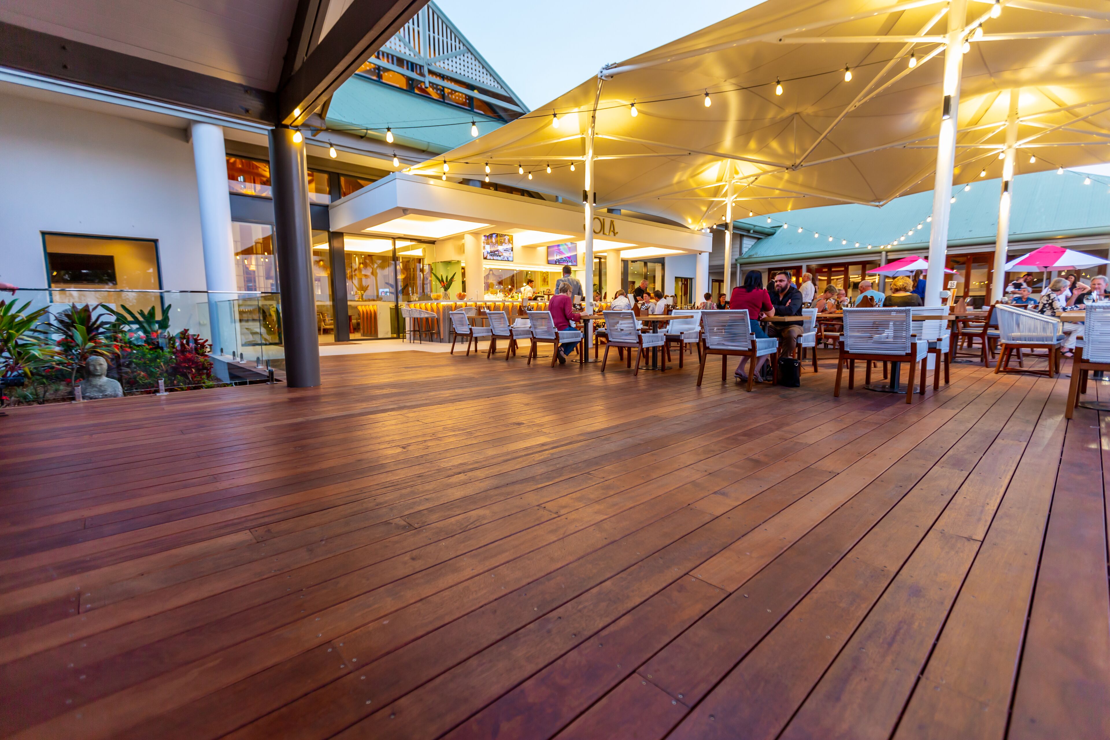 An outdoor dining area with wooden flooring, tables, and chairs under large umbrellas.