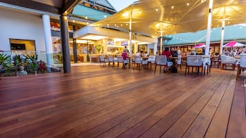 An outdoor dining area with wooden flooring, tables, and chairs under large umbrellas.