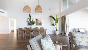 A spacious living area with a high ceiling, a dining table with chairs, a sofa, and a large potted plant.