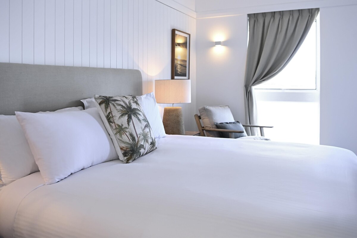 Habitación de hotel con una cama grande, una silla, una lámpara y una ventana con cortinas.