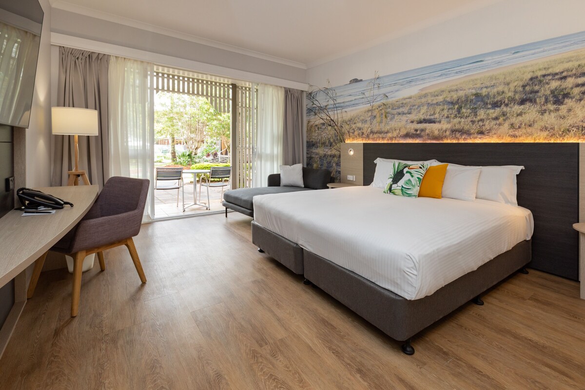 Habitación de hotel con cama, escritorio, silla y vistas al exterior.