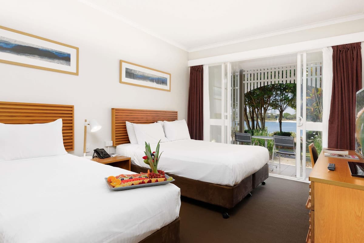 A hotel room with two beds, a desk, and a balcony with a view of the sea.