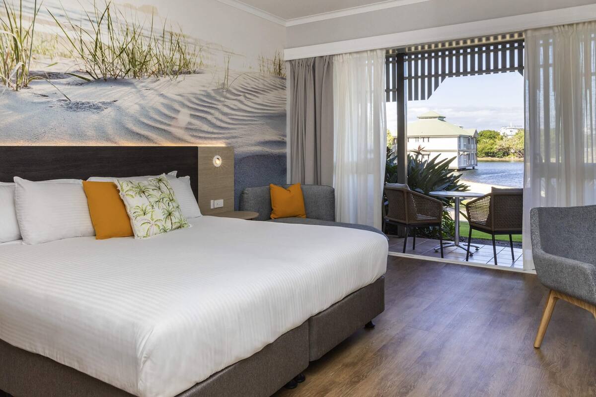 A hotel room with a large bed, a sofa, a dining area, and a view of the water.