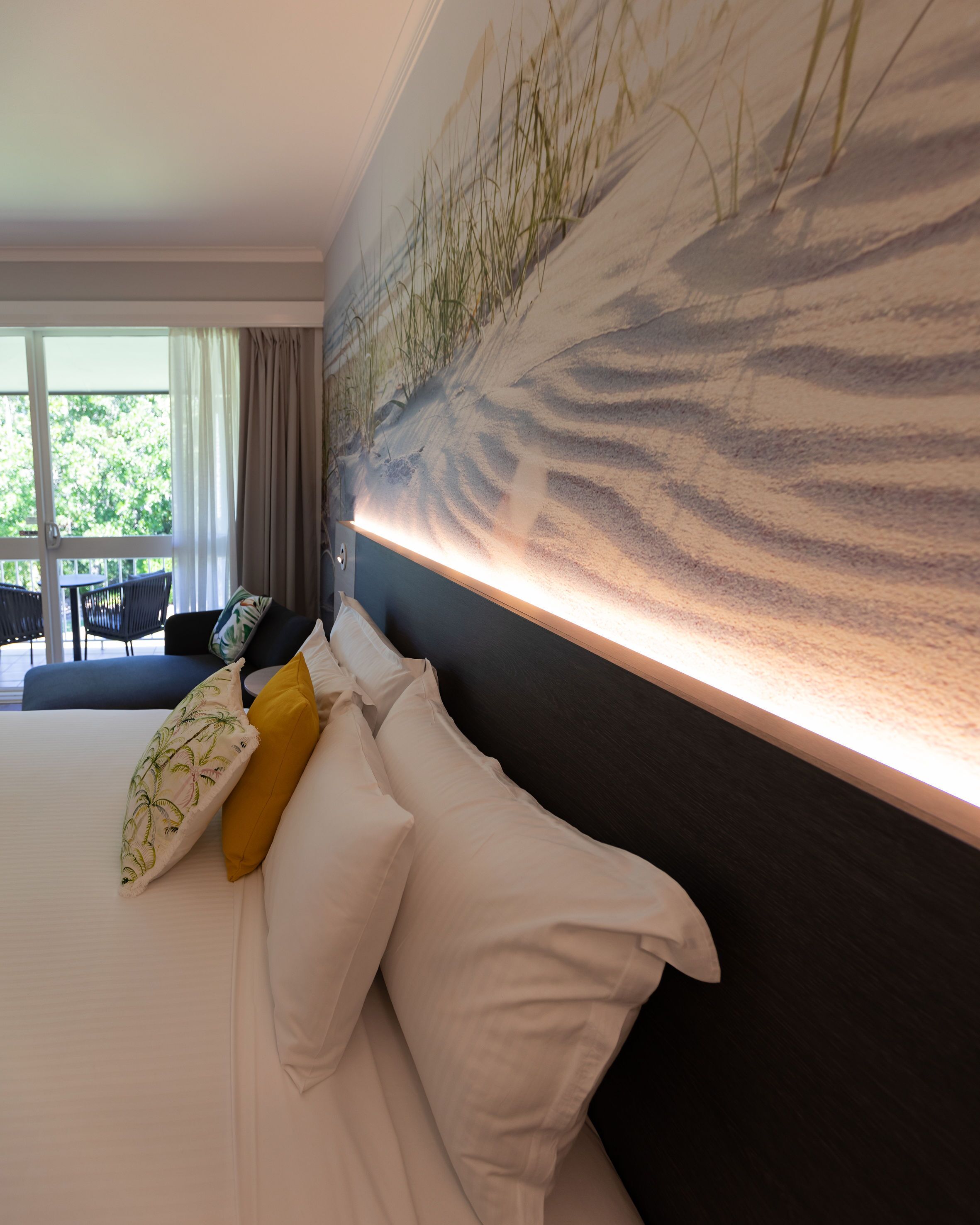 A hotel room with a large bed, a view of greenery through the window, and a modern wall design.