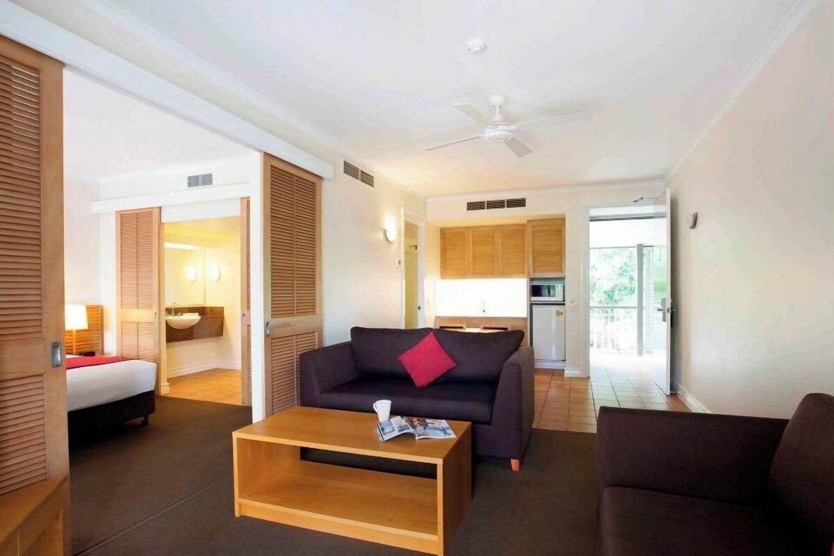 Una habitación de hotel con cama, sofá, mesa de centro, ventilador de techo y kitchenette.