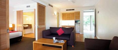 Una habitación de hotel con cama, sofá, mesa de centro, ventilador de techo y kitchenette.