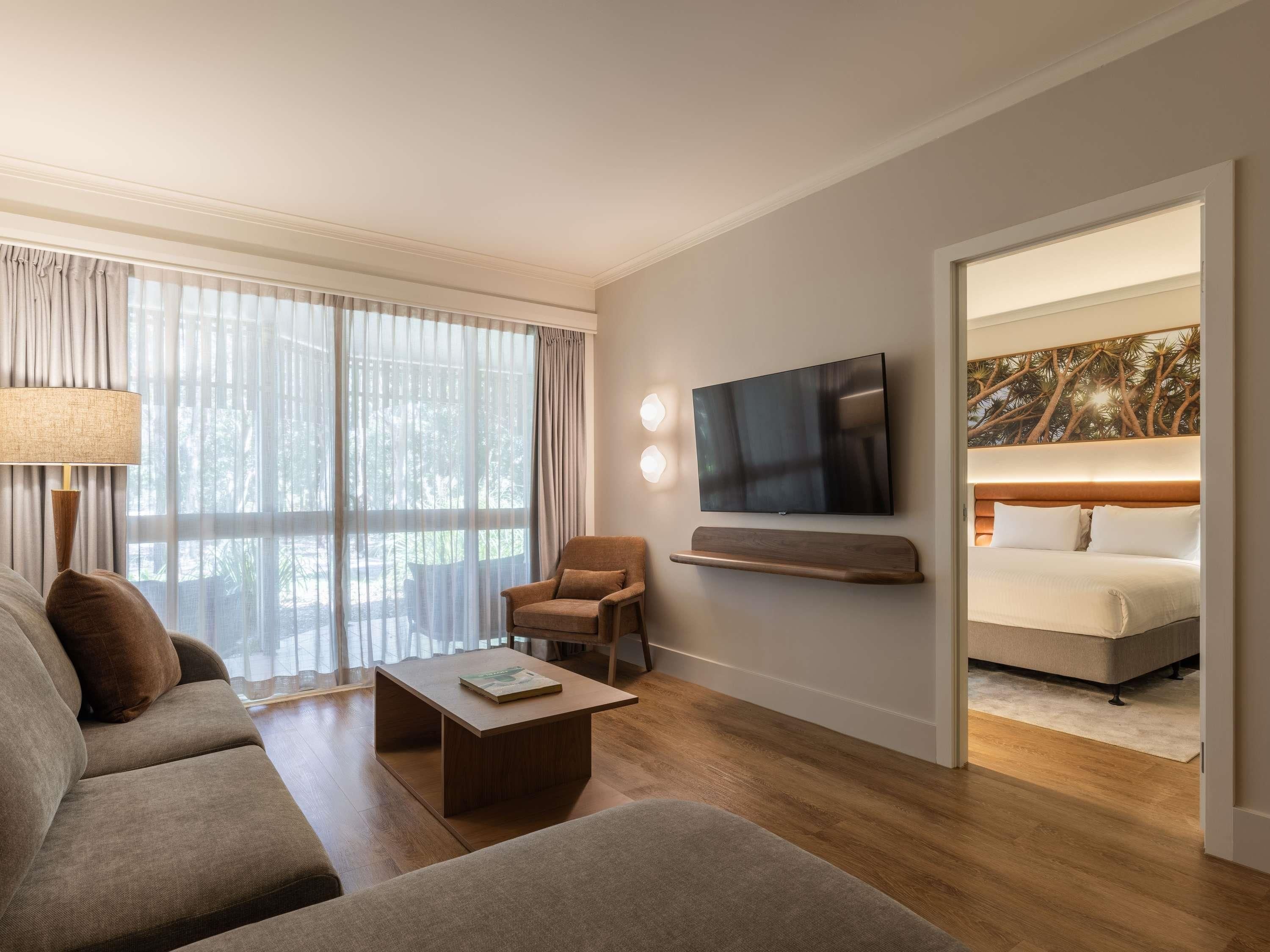 Une chambre d’hôtel moderne équipée d’un canapé, d’un fauteuil, d’une table basse, d’un téléviseur à écran plat et d’un lit avec une tête de lit.