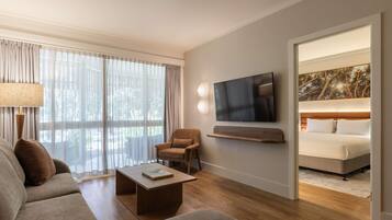 Une chambre d’hôtel moderne équipée d’un canapé, d’un fauteuil, d’une table basse, d’un téléviseur à écran plat et d’un lit avec une tête de lit.