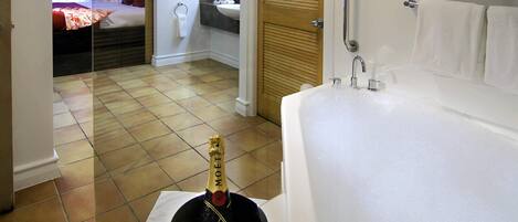 A bathroom with a bathtub, a sink, and a shower. There is a bottle of champagne in a bucket on the floor.