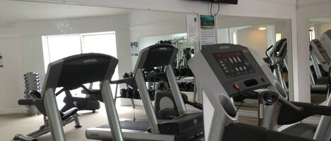 A gym with treadmills, weight machines, and a television mounted on the wall.