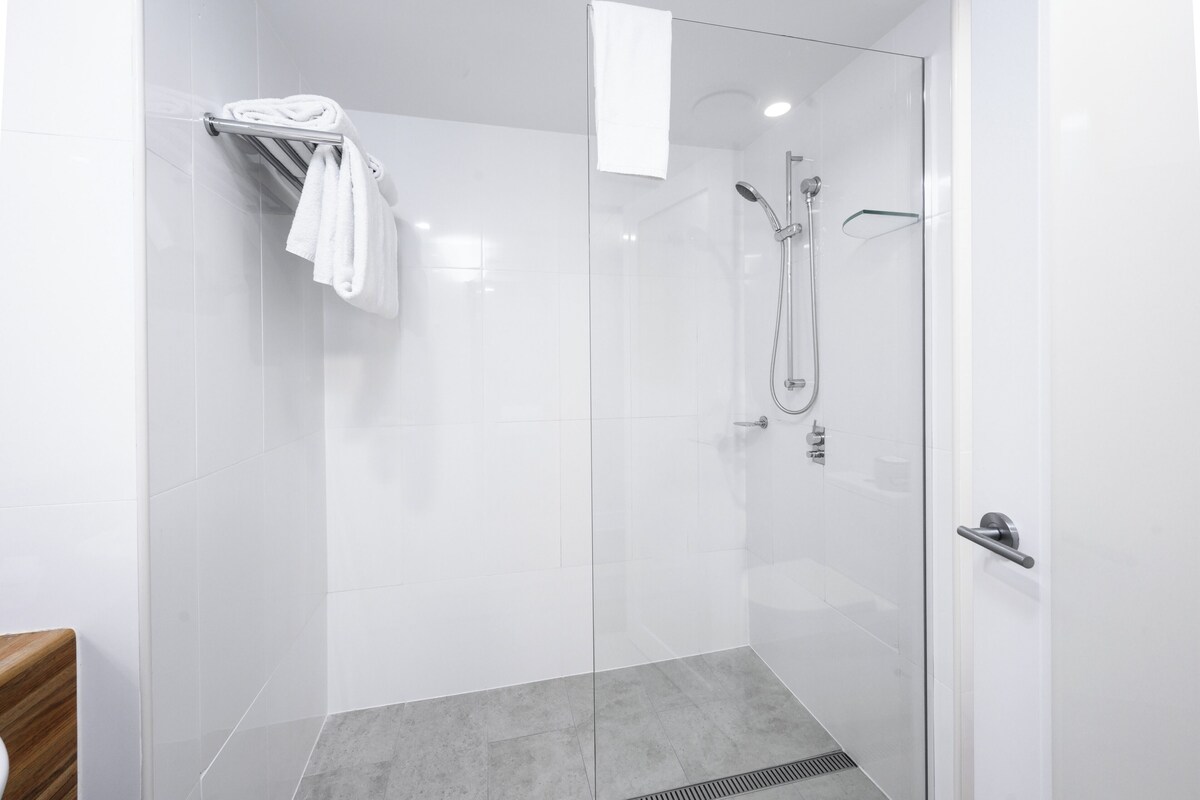 Un baño moderno con cabina de ducha de vidrio, un perchero y un cabezal de ducha.