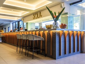 Un espace bar agrémenté d’une enseigne « SOLA », de tabourets de bar modernes et d’un comptoir où sont exposés divers articles.