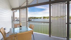 A glass-top table with wicker chairs on a deck with a view of a lake and docked boats.